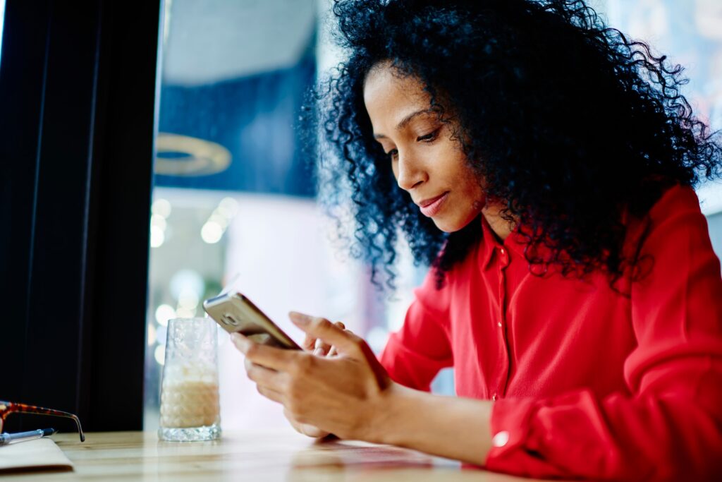 Black woman sitting at table of coffee shop and text messaging