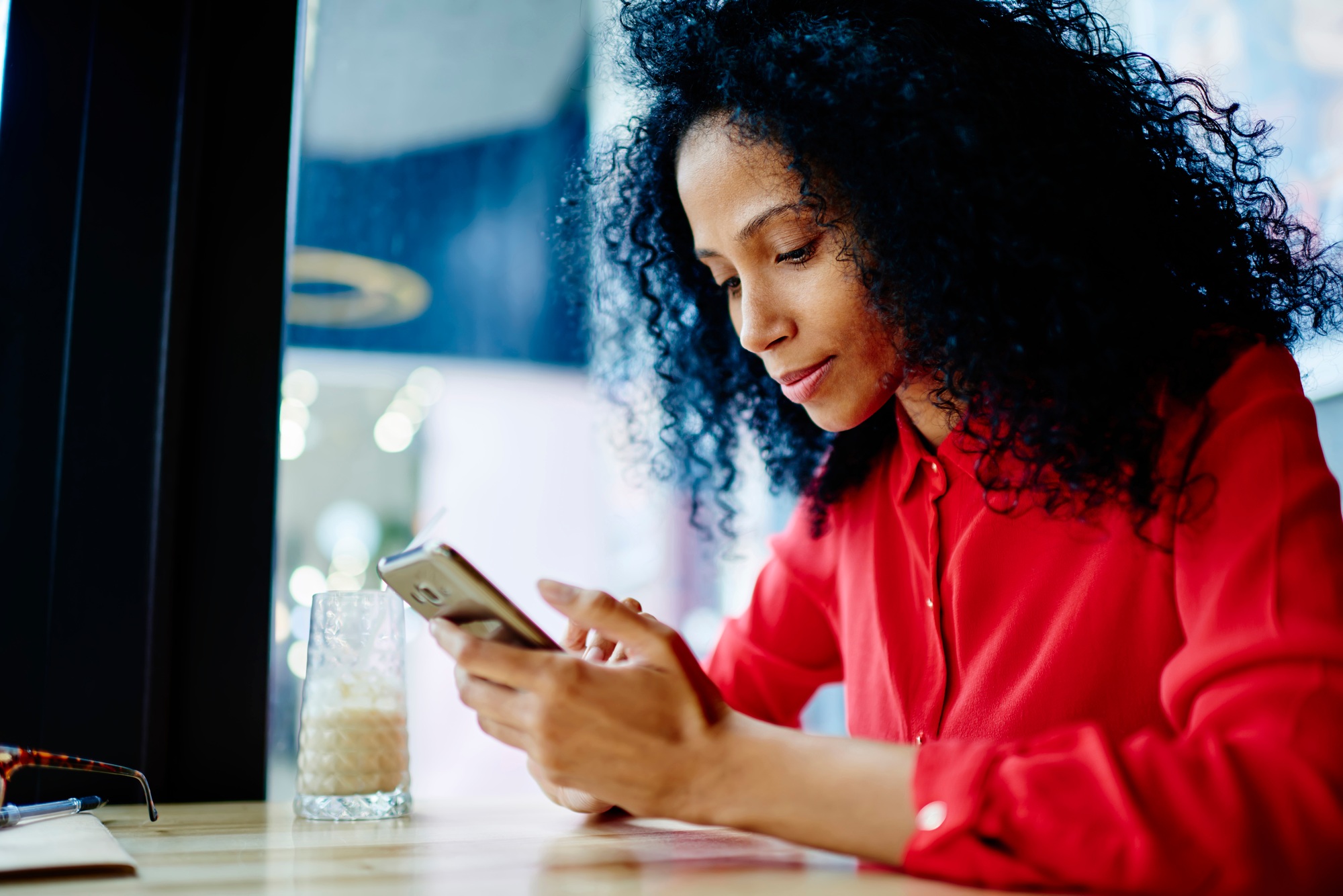 Black woman sitting at table of coffee shop and text messaging