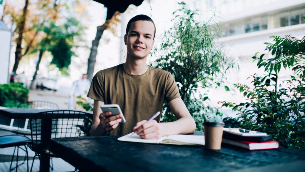 Joyful man writing in notebook in cafe