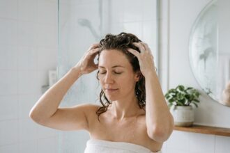 Femme aux cheveux ondulés appliquant un shampoing sans sulfate dans une salle de bain minimaliste