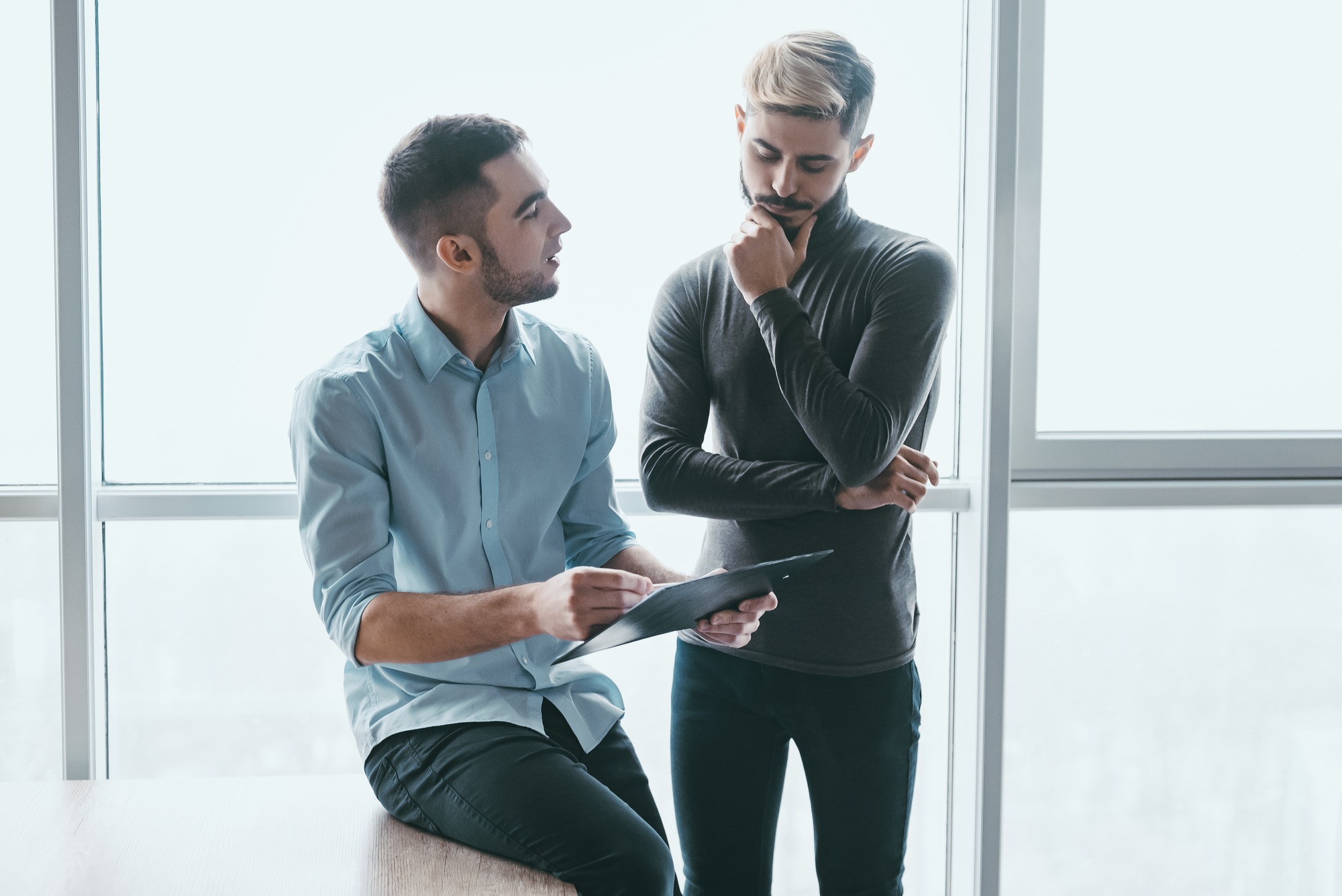Two focused male co-workers deep in discussion together, while standing in a modern office